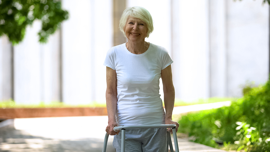 Cheerful Senior Woman With Walking Frame Looking At Camera Outdo