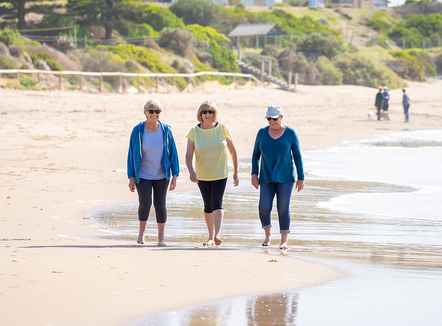 Three Happy Senior Women Walking And Exercising Together On Beac